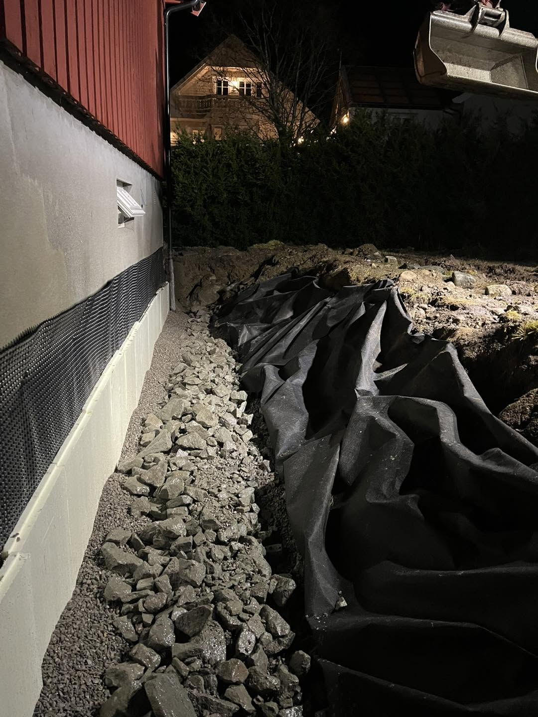 Gravemaskin graver dreneringsgrøft langs bustad