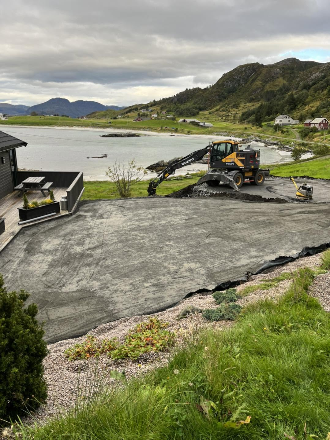 Planering av uteareal ved sjøen med gravemaskin og strand i bakgrunnen