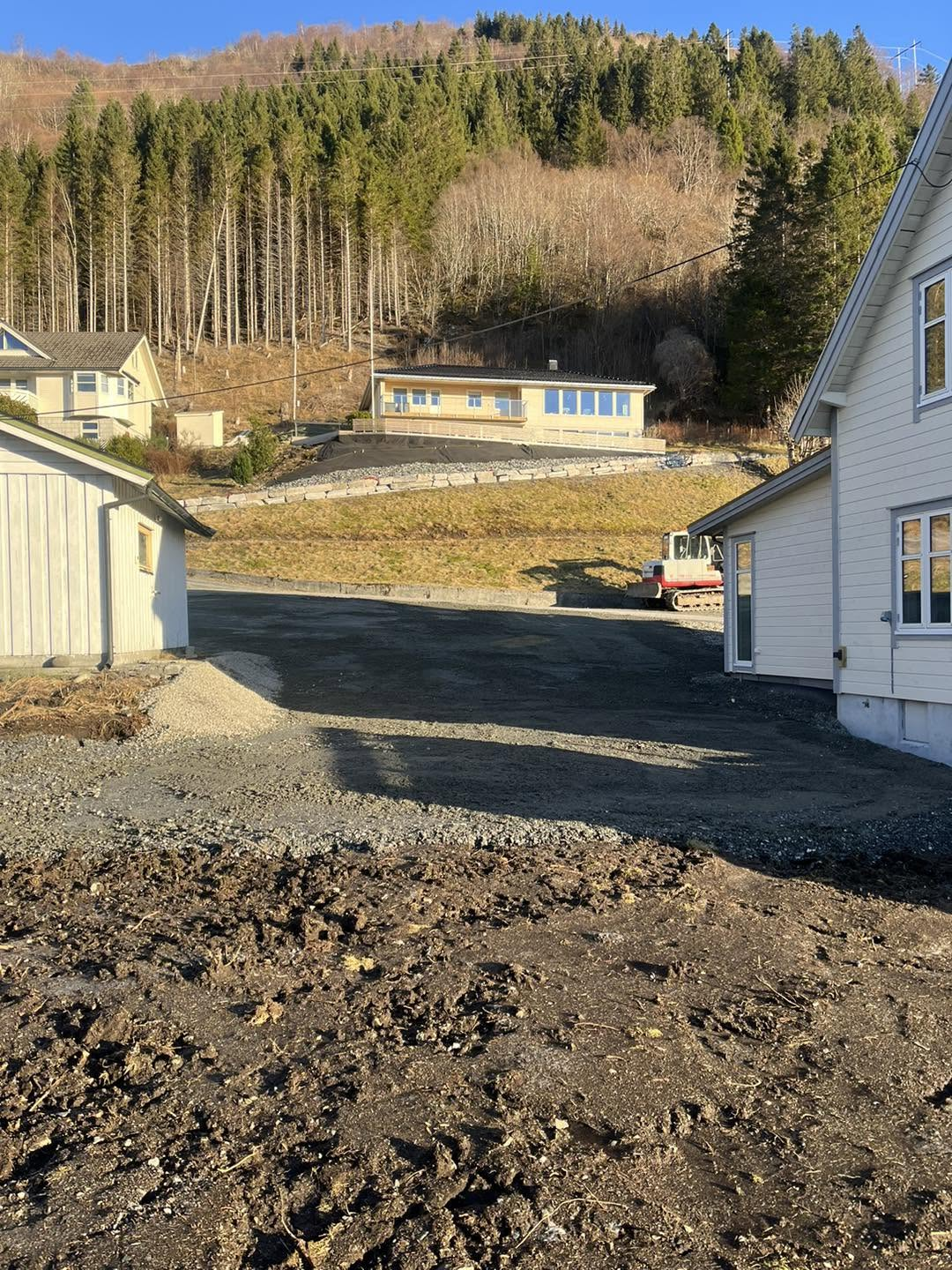 Planert og gruslagt uteareal mellom husa med skogkledd li i bakgrunnen
