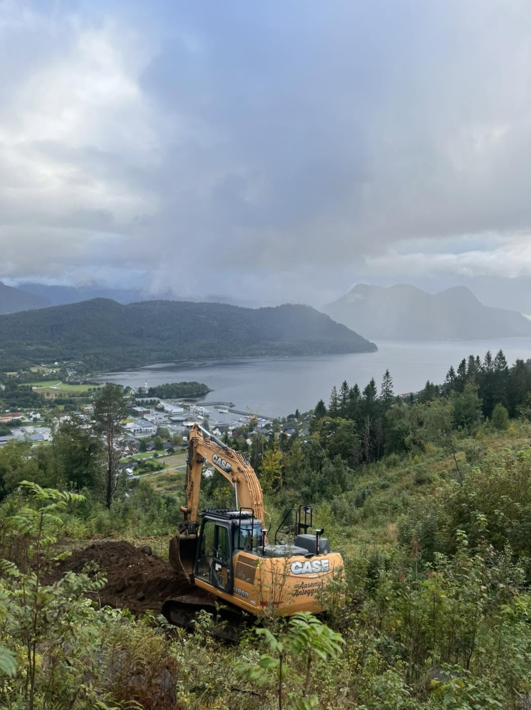 Gravemaskin rydder bratt tomt med utsikt over Volda og fjorden