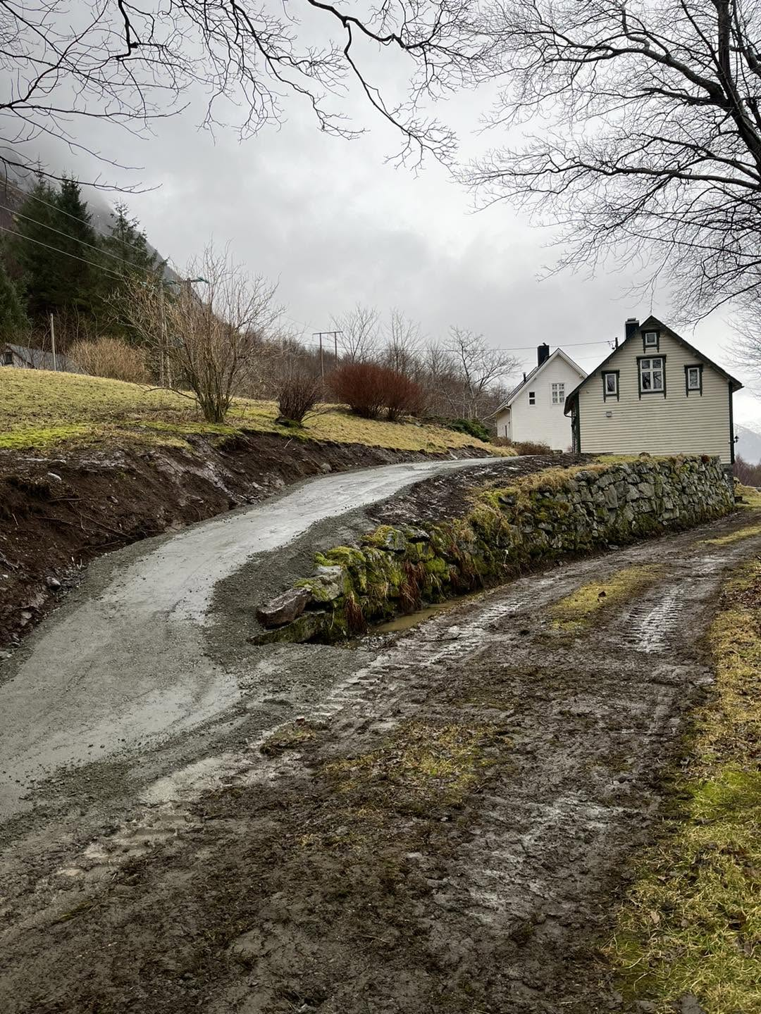 Gammal gjørmete gardsveg under oppgradering ved den gamle steinmuren og gardshusa