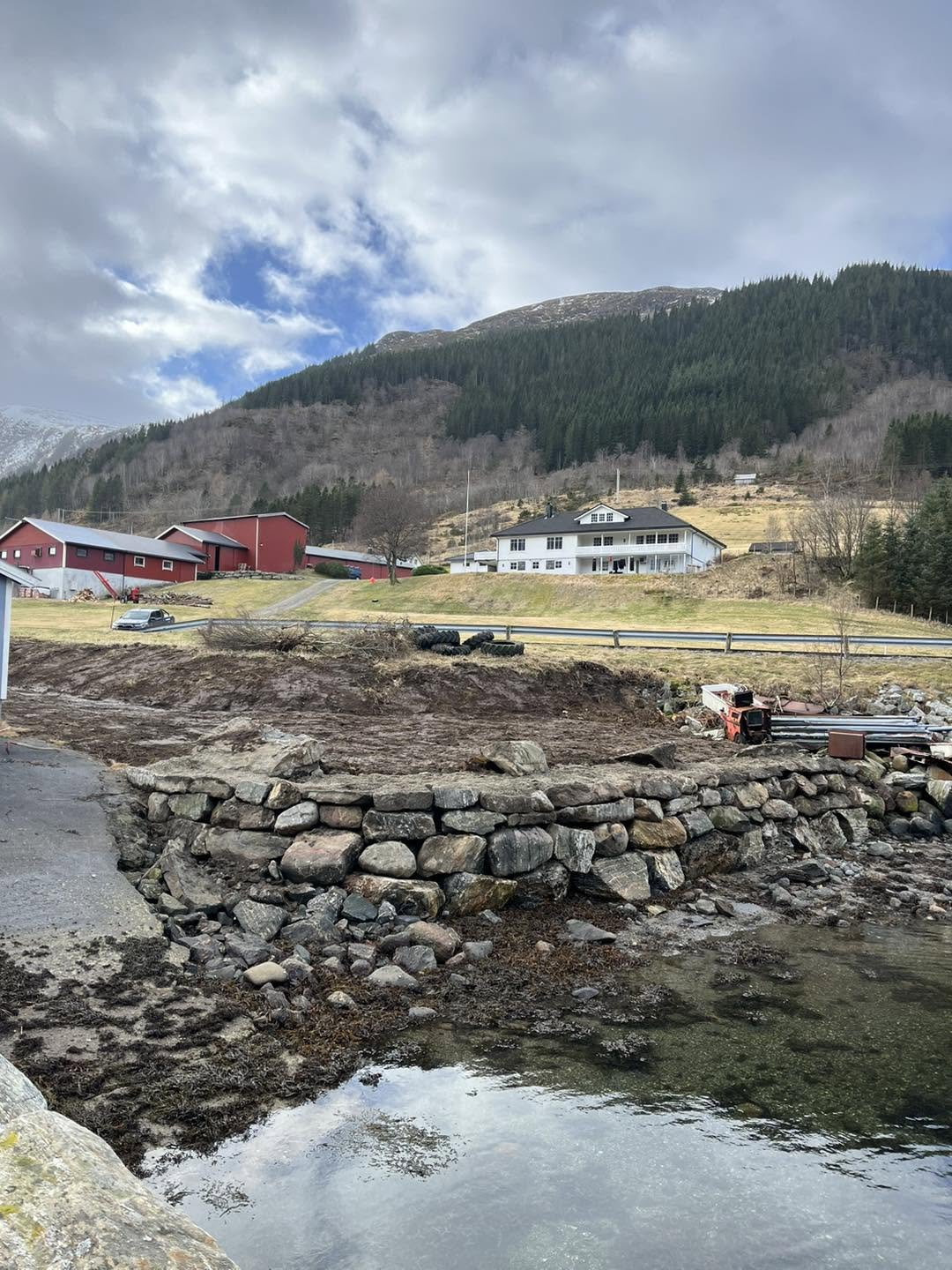 Restaurert steinkai ved fjorden med gard og fjell i bakgrunnen
