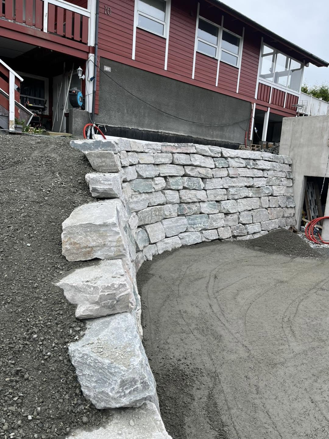 Natursteinsmur i terrasse opp mot raud bustad og garasje