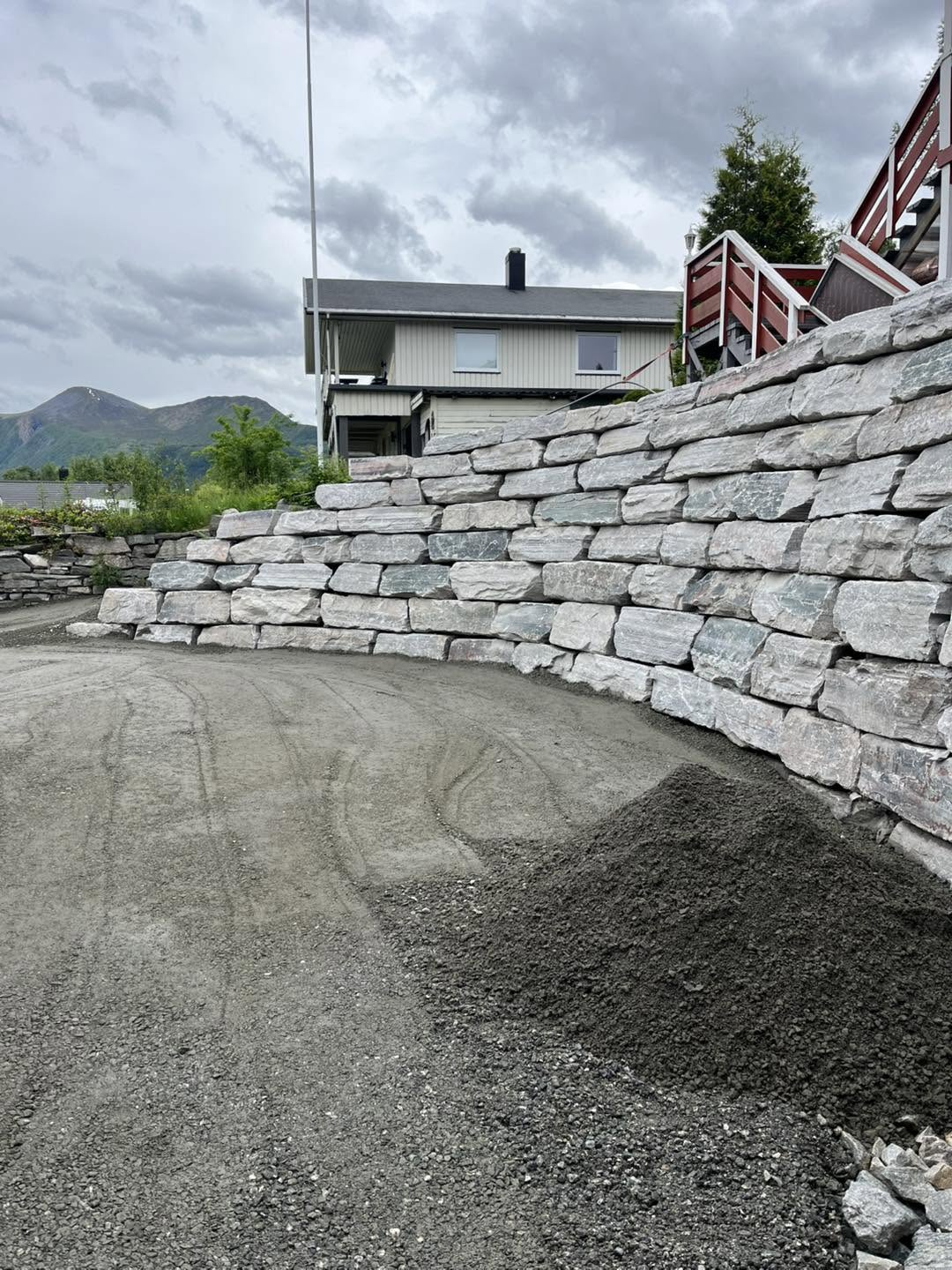 Ferdig gruslagt uteareal framfor den store bua natursteinsmuren ved bustaden