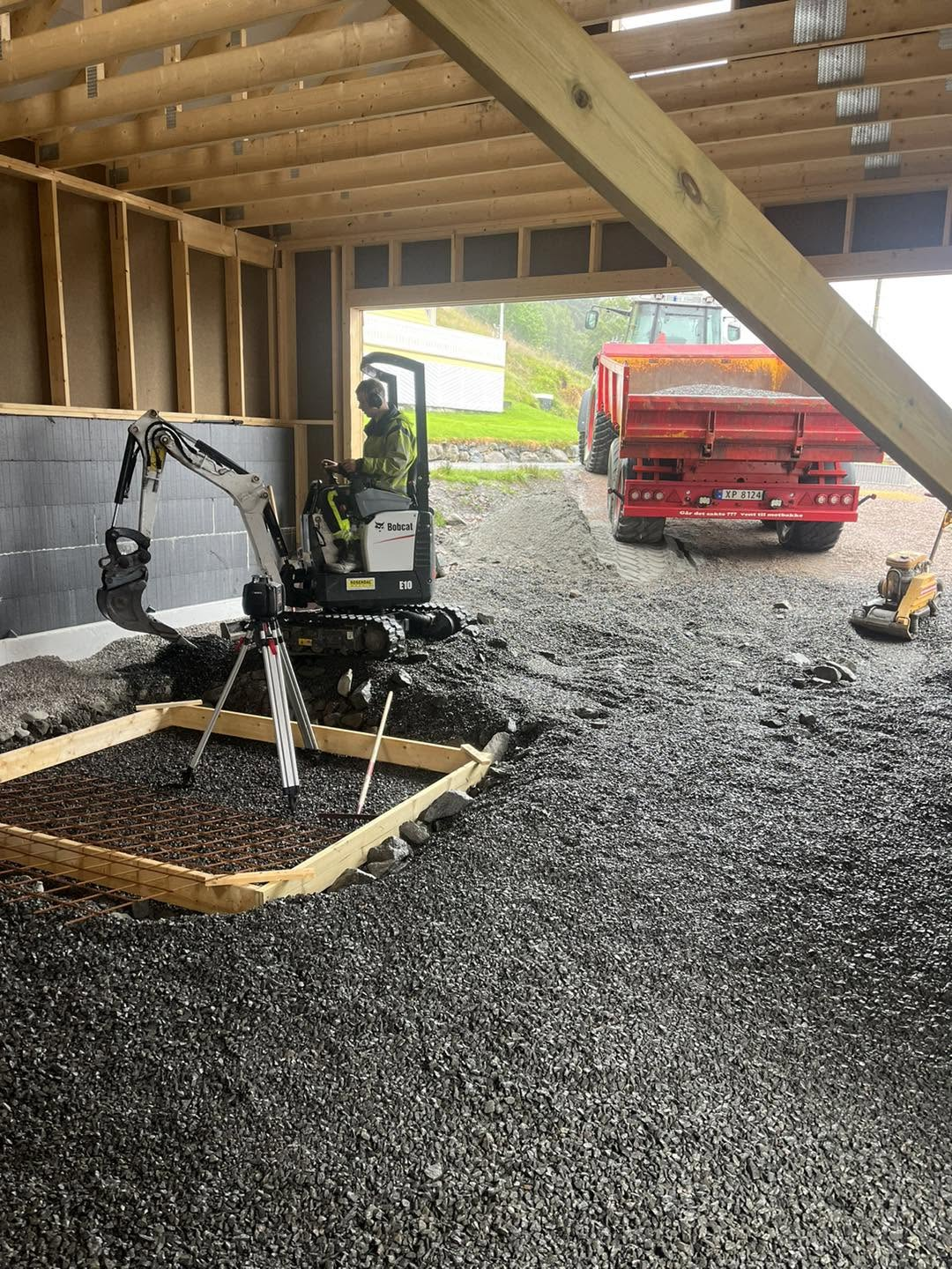 Minigravemaskin planerar grus med grustransport utanfor garasjen