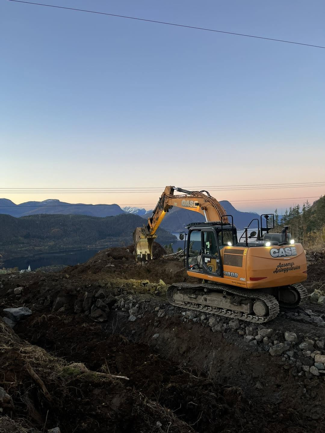 Gravemaskin frå Aasemyr Anleggsservice i arbeid i bratt fjellterreng over fjorden