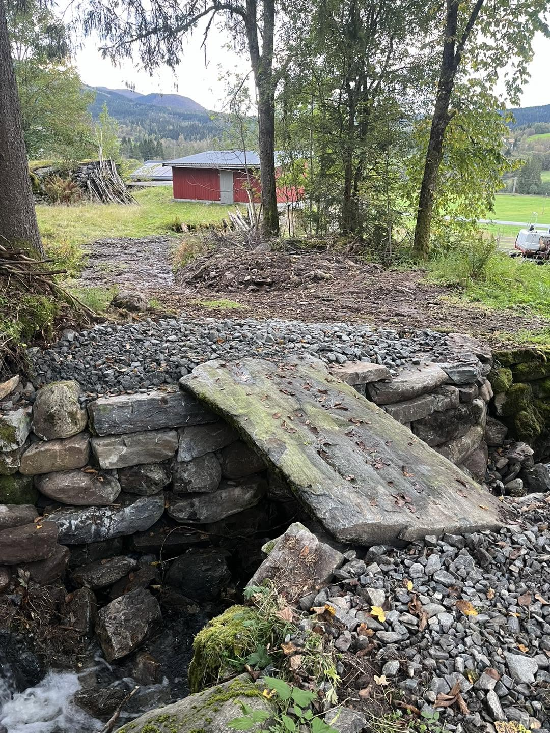 Restaurert steinmur med ny bruplate og gruslagt flate over bekken