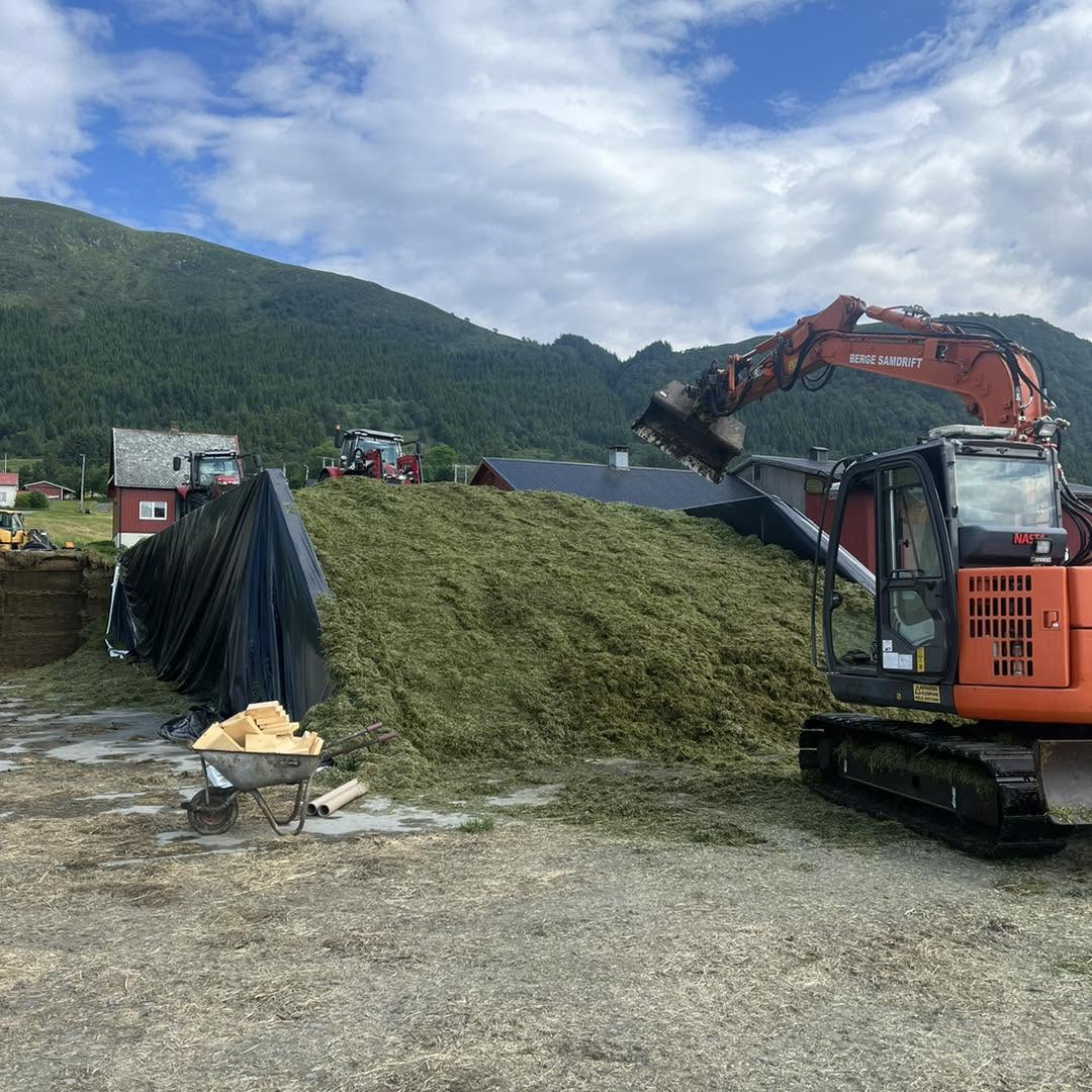 Gravemaskin arbeider med stor fôrhaug for silo på garden