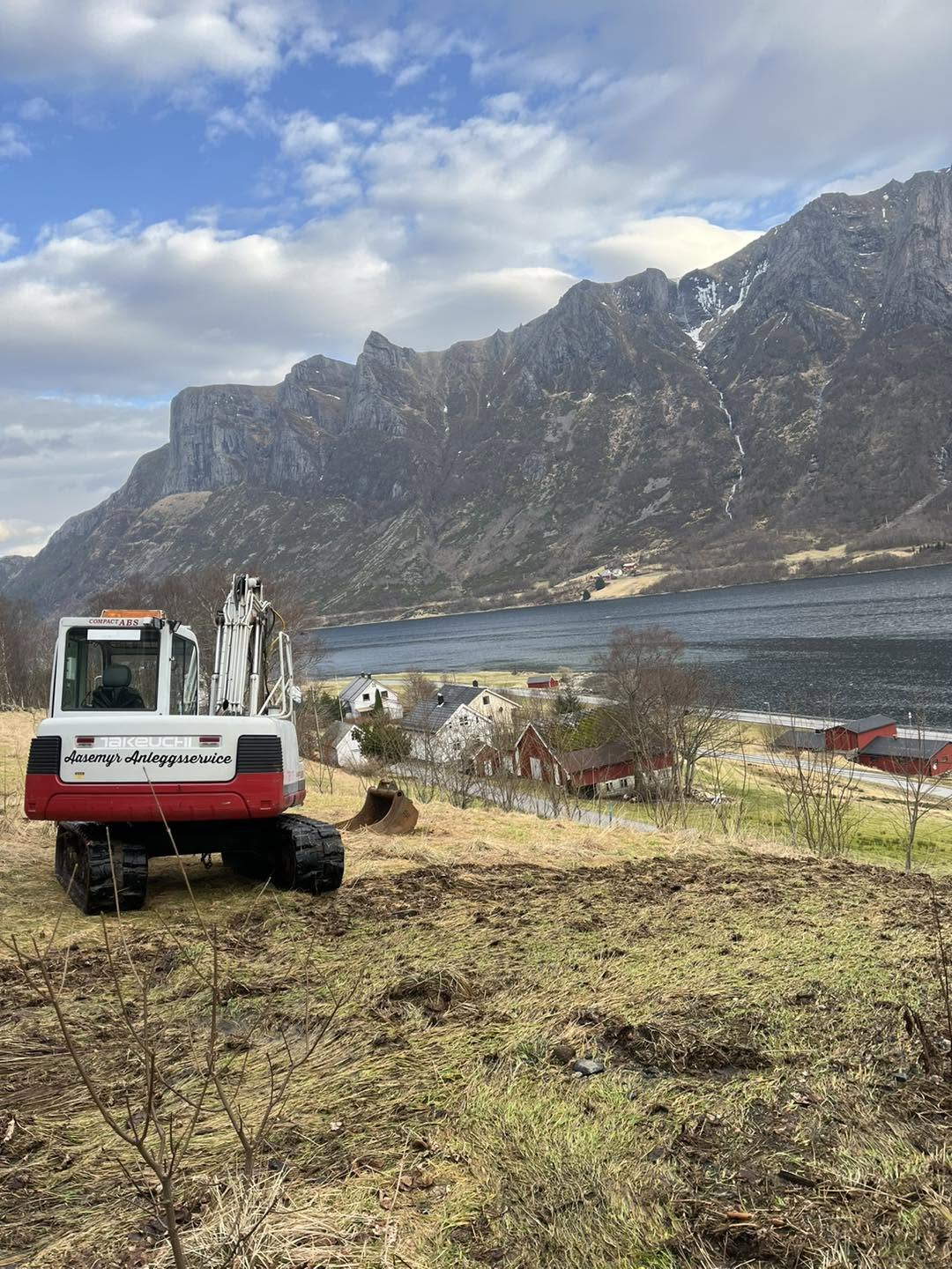 Gravemaskin på planert bakke med utsikt over fjorden og fjell